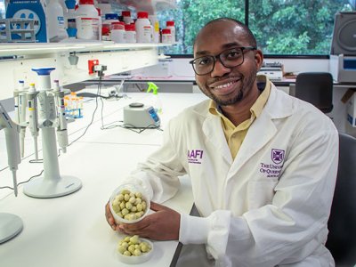 a man in a white lab coat sits at a bench holding a container of small round green fruit